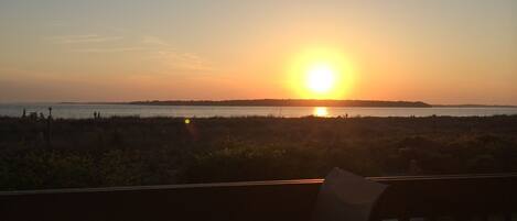 A sunset view from a balcony overlooking a body of water with distant land visible.