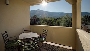 A balcony with a table and chairs, a view of mountains, and a clear sky.