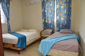 Habitació amb dos llits, una cadira i una finestra amb cortines.