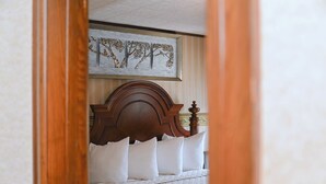 A bedroom with a wooden headboard, a large painting of trees, and a neatly made bed with white bedding. - The Copper Penny House - Walking Distance To The Falls! (Niagara Falls)