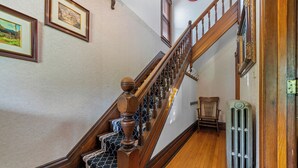 A wooden staircase with a patterned carpet, a radiator, and framed pictures on the walls. - The Copper Penny House - Walking Distance To The Falls! (Niagara Falls)