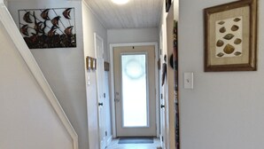 A hallway with wooden flooring, white walls, and a ceiling with wooden beams. There are framed pictures on the walls and a door at the end of the hallway. - Trout Quarters! Beautiful 2 bedroom, 2.5 bath! Walk to the Beach! (Port Aransas)