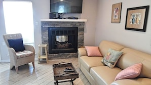 A living room with a fireplace, a sofa, a chair, and a television mounted above the fireplace. - Trout Quarters! Beautiful 2 bedroom, 2.5 bath! Walk to the Beach! (Port Aransas)