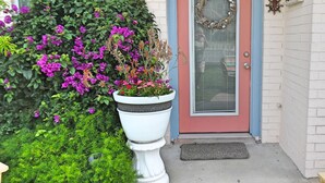 A house with a red door, a white porch, and a large planter with purple flowers. - Trout Quarters! Beautiful 2 bedroom, 2.5 bath! Walk to the Beach! (Port Aransas)