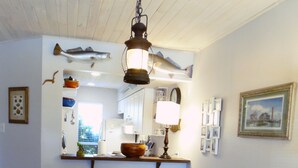 A dining area with a wooden table and white chairs, a hanging fish decoration, and a pendant light. - Trout Quarters! Beautiful 2 bedroom, 2.5 bath! Walk to the Beach! (Port Aransas)