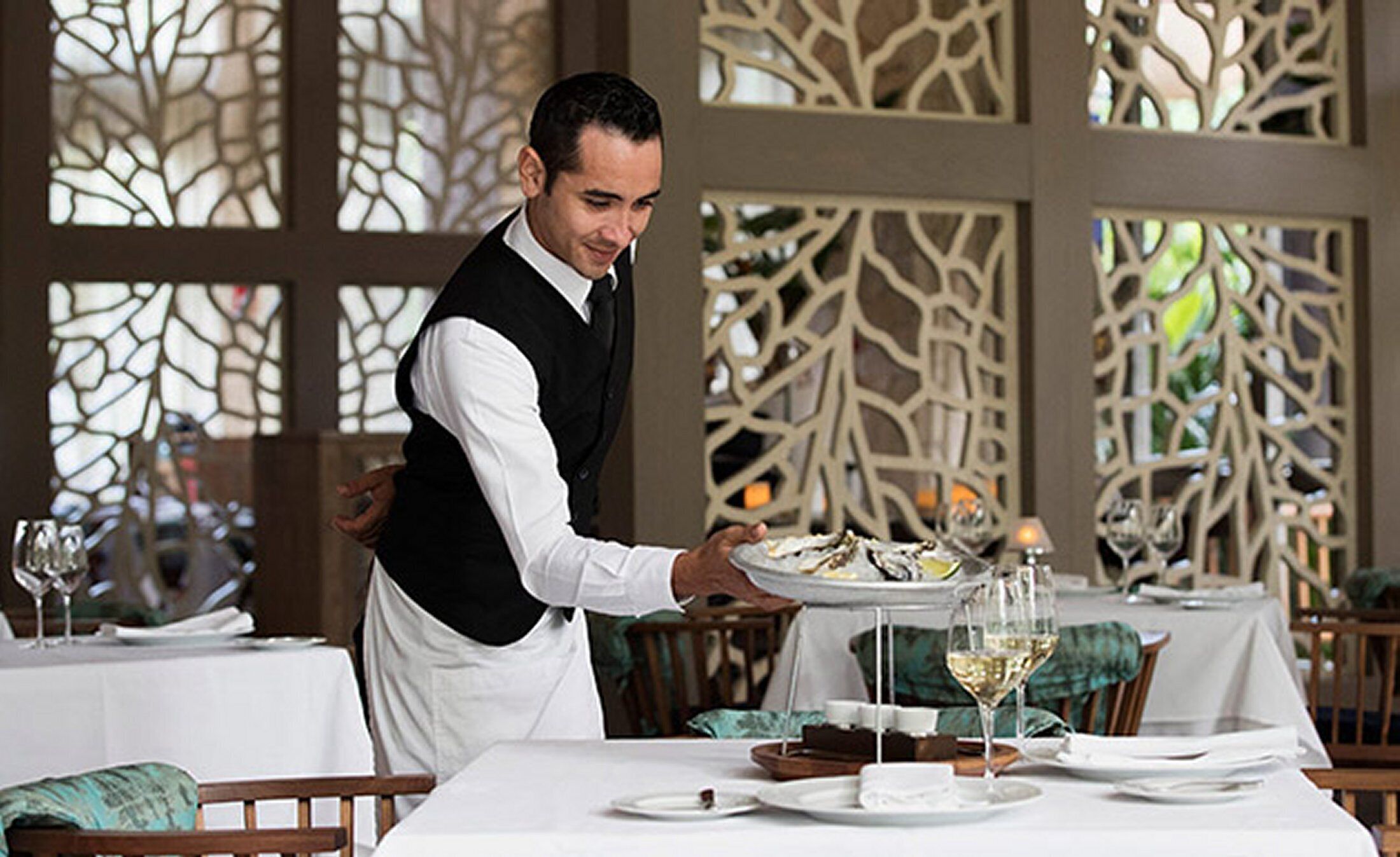 Un serveur apporte des plats à une table dans un restaurant décoré de paravents et recouvert de nappes blanches.