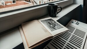 A window with a view of a cityscape, a book, and a black mug on a windowsill. - AthinA STREETAPARTMENTS (Athens)