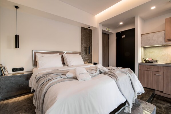 A modern hotel room with a neatly made bed, a bedside table, a small seating area, and a kitchenette. - AthinA STREETAPARTMENTS (Athens)