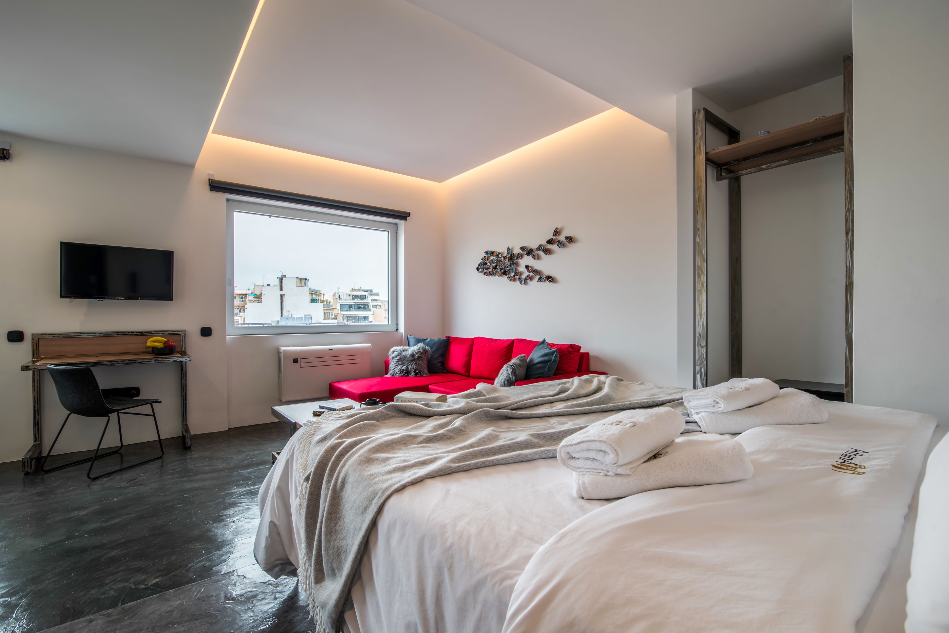 A modern hotel room with a bed, a desk, a TV, and a window with a city view.