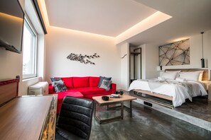 A modern living room with a red sofa, a black leather chair, a wooden coffee table, and a bed with white bedding. - AthinA STREETAPARTMENTS (Athens)