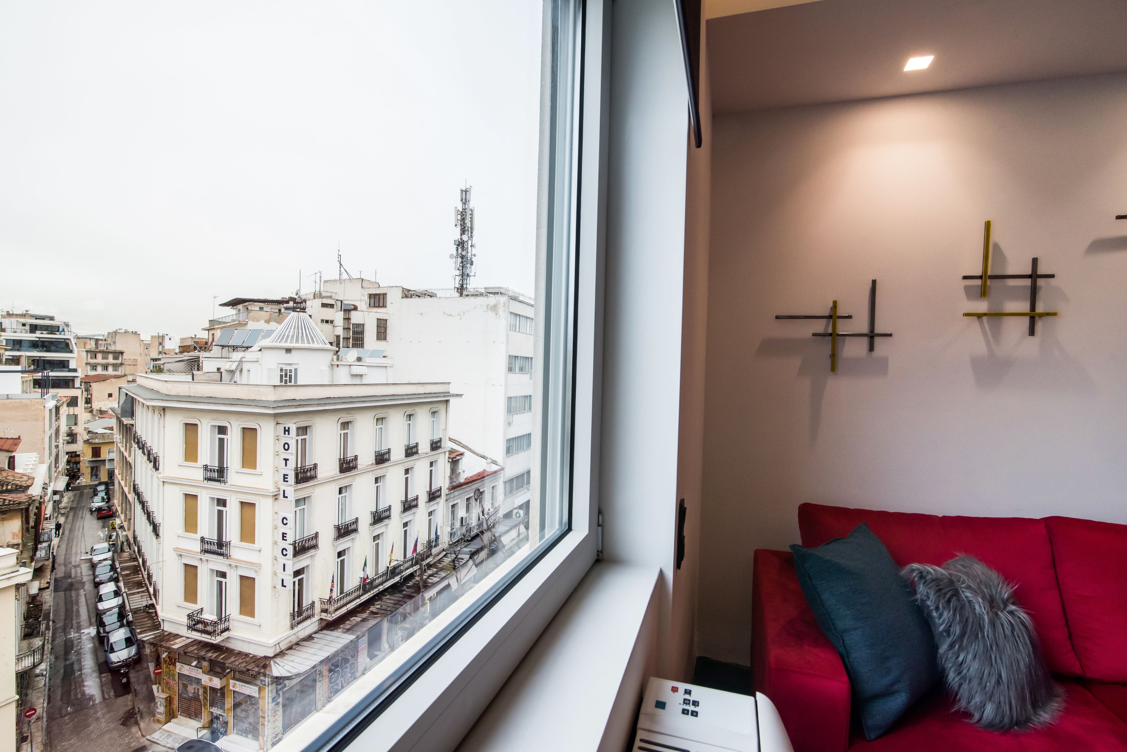 Ein Hotelzimmer mit großem Fenster und Blick auf die Stadtlandschaft, einem roten Sofa und einer Wand-Klimaanlage.