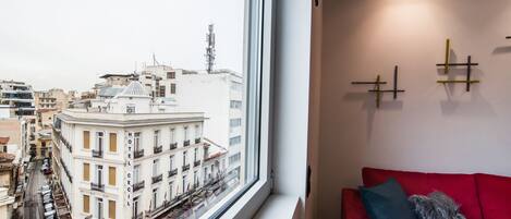 Ein Hotelzimmer mit großem Fenster und Blick auf die Stadtlandschaft, einem roten Sofa und einer Wand-Klimaanlage.