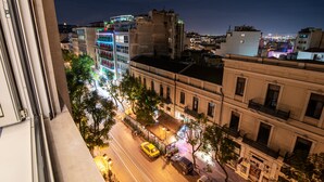 A nighttime cityscape with illuminated buildings, a street with cars, and a view from a window overlooking the urban area. - AthinA STREETAPARTMENTS (Athens)