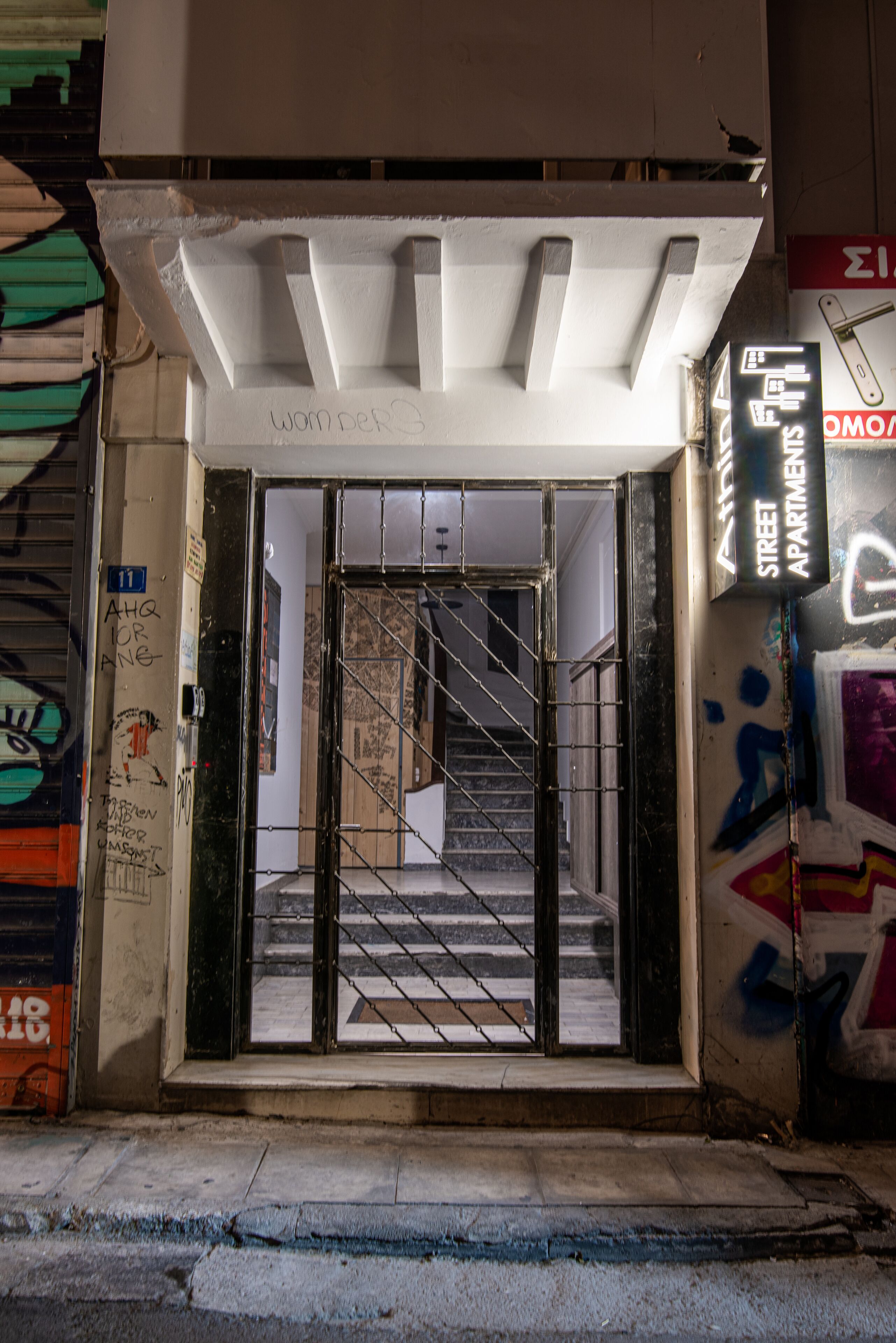 Ein Gebäudeeingang mit einem Metallgitter, einer zur Innenseite führenden Treppe und Graffiti an den Wänden.