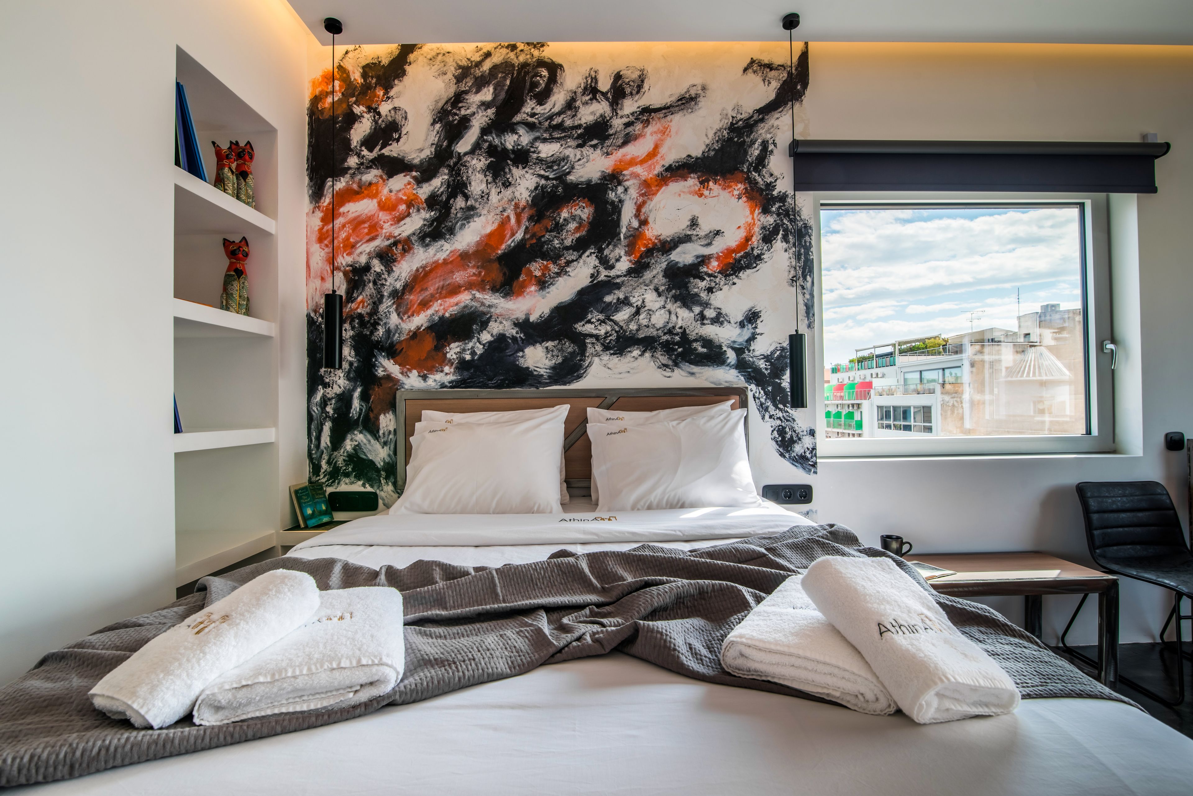 A modern hotel room with a large bed, a city view, and a unique abstract wall art.