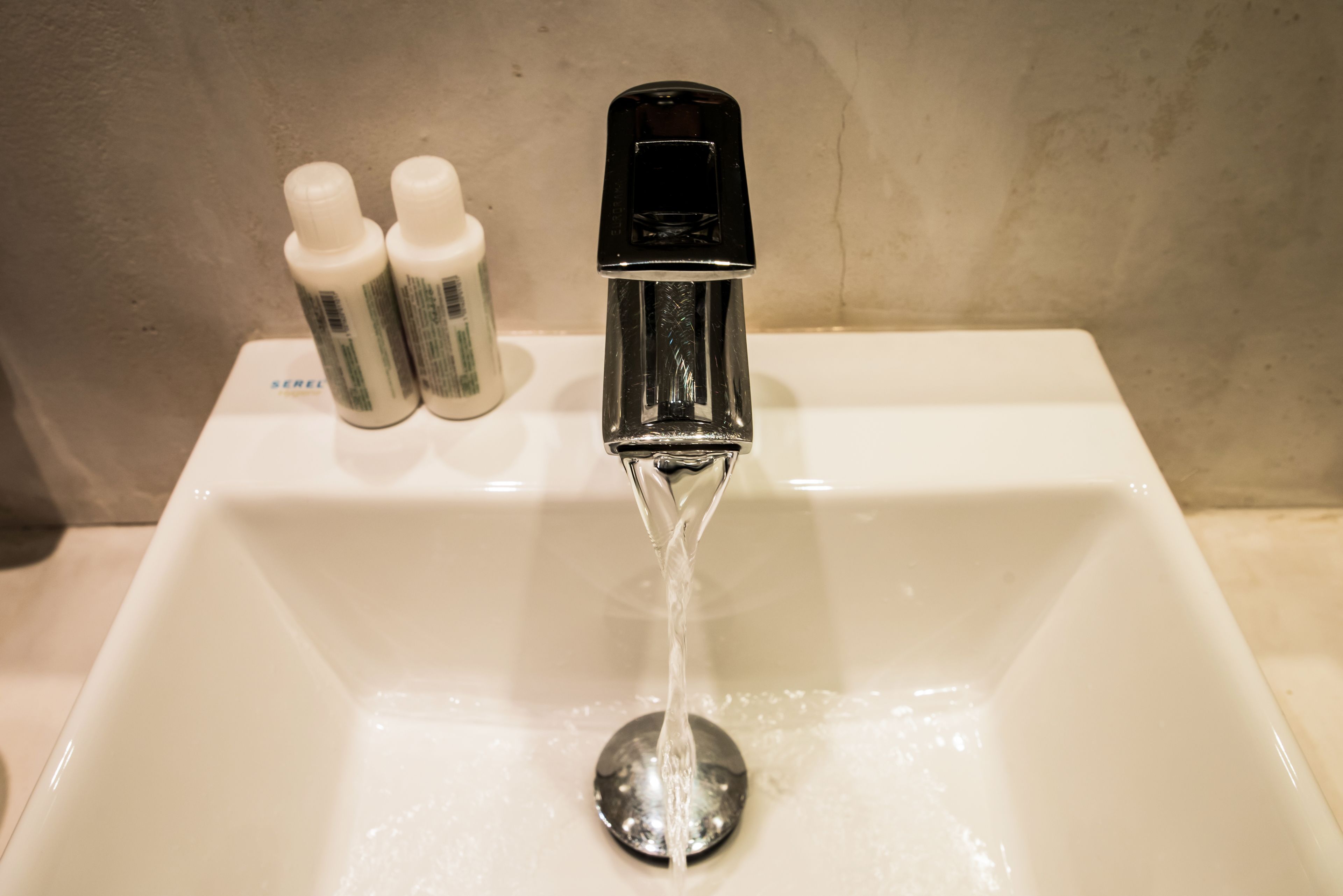 A white bathroom sink with a chrome faucet and two bottles of hand soap on the countertop.