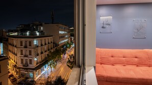 A hotel room with a large window overlooking a city street at night, a bed, and two framed artworks on the wall. - AthinA STREETAPARTMENTS (Athens)