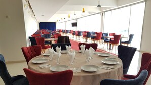 Comedor con mesas redondas dispuestas para cuatro personas, rodeado de sillas tapizadas en rojo y azul.