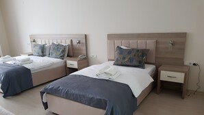 A hotel room with two beds, each with a bedside table, a phone, and a lamp. The room has a wooden headboard and a light-colored floor.