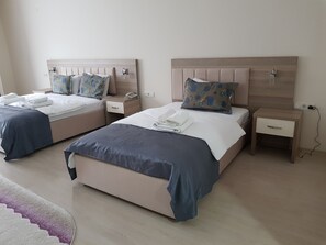 Habitación de hotel con dos camas, cada una con una mesita de noche, teléfono y lámpara. La habitación tiene un cabecero de madera y piso de color claro.