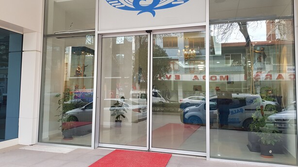Entrada de hotel con un amplio ventanal de vidrio, alfombra roja y un logotipo sobre las puertas.