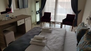 Habitación de hotel con cama, escritorio, silla, televisión y ventana con cortinas.
