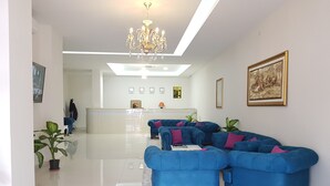 Un moderno hall de hotel con mostrador de recepción, sofás azules, una lámpara de araña y una gran obra de arte enmarcada en la pared.