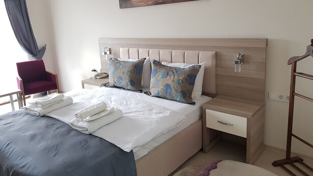 A neatly made bed with a blue bedspread and white pillows, a wooden headboard, a nightstand with a lamp, and a painting of trees on the wall.