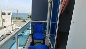 Un balcon avec deux fauteuils bleus dotés de coussins, une balustrade en verre et une vue sur la mer.
