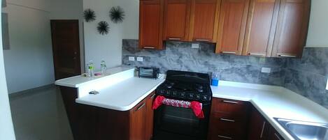 Una cocina con armarios de madera, estufa negra, encimera blanca y salpicadero de azulejos.