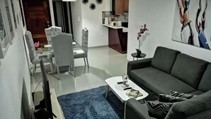 Un salon moderne avec un canapé gris, une table basse et un coin repas comprenant une table et des chaises blanches.