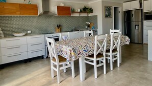 A modern kitchen with white cabinetry, a tiled backsplash, a stainless steel refrigerator, and a dining table with chairs. - SeaEsta@Culburra- 3min walk to the Beach or Curleys Bay (Culburra Beach)