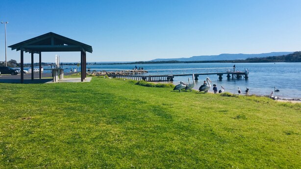 A gazebo, grassy area, and a pier extending into a lake with mountains in the background. - SeaEsta@Culburra- 3min walk to the Beach or Curleys Bay (Culburra Beach)