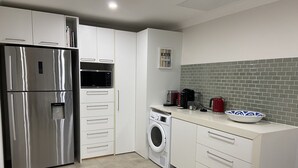 A modern kitchen with stainless steel appliances, a washing machine, and a coffee maker. - SeaEsta@Culburra- 3min walk to the Beach or Curleys Bay (Culburra Beach)