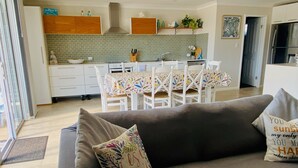 A modern kitchen with white cabinets, a tiled backsplash, and a dining area with a table set for four. - SeaEsta@Culburra- 3min walk to the Beach or Curleys Bay (Culburra Beach)