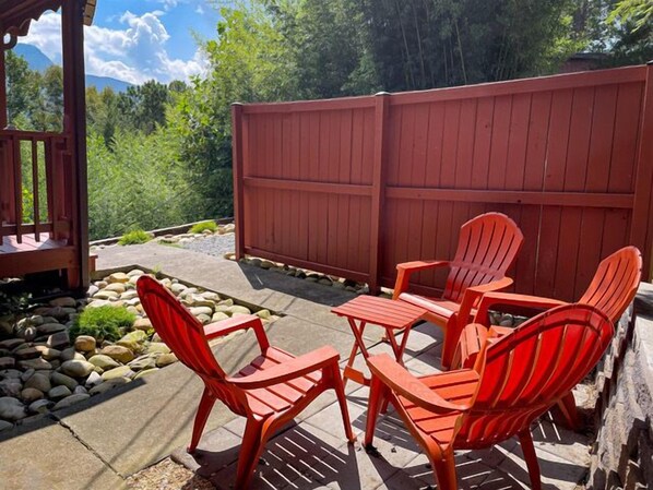 Een terras met rode Adirondack-stoelen en een tafel, omgeven door een houten omheining en een pad van stenen.