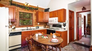 A kitchen with wooden cabinets, a microwave, a sink, and a dining table set with plates and cups. - Gatlinburg Log Cabin, Amazing Views Hot Tub, Theater Room, Internet Free Tickets (Gatlinburg)