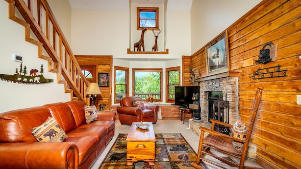 A cozy living room with a leather sofa, a wooden rocking chair, a fireplace, and a staircase. - Gatlinburg Log Cabin, Amazing Views Hot Tub, Theater Room, Internet Free Tickets (Gatlinburg)
