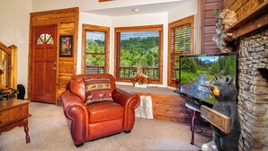 A cozy living room with a leather sofa, a television, and a stone fireplace. - Gatlinburg Log Cabin, Amazing Views Hot Tub, Theater Room, Internet Free Tickets (Gatlinburg)