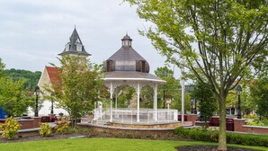 A gazebo with a white fence and a dome roof, surrounded by a well-maintained lawn and trees.