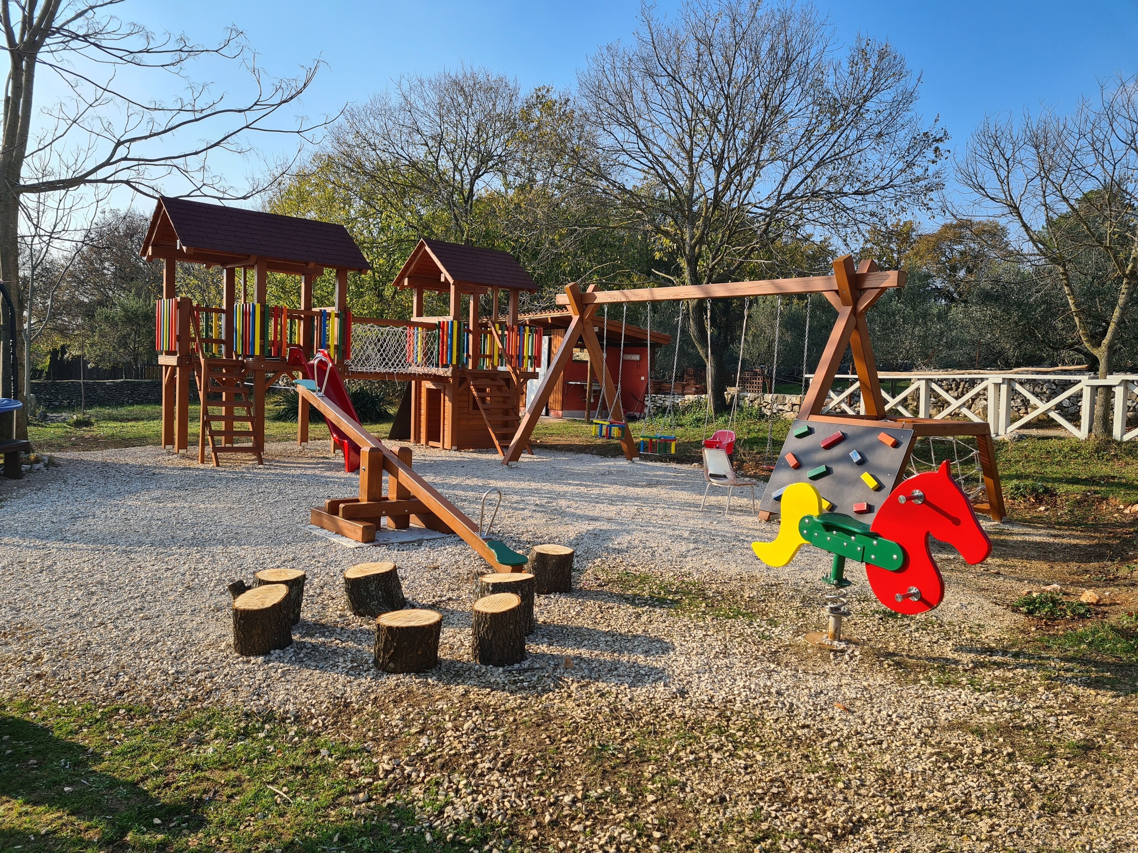 Een speeltuin met houten speeltoestellen, schommels en een klimgebied.