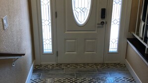 Puerta blanca con un panel de vidrio y dos ventanas verticales, que da a un suelo de baldosas con diseño geométrico.