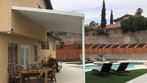 Un patio con piscina, mobiliario exterior y una zona de estar cubierta.