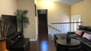 Una sala de estar con televisión, sofá, mesa de centro y escalera.