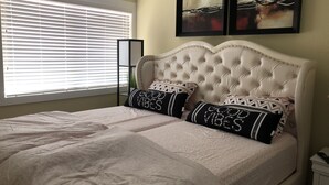 Un dormitorio con una cama grande, dos almohadas decorativas, un cabecero y dos obras de arte enmarcadas en la pared.