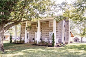 Une cabane en bois dotée d’une véranda, de chaises blanches et d’une cheminée en pierre.