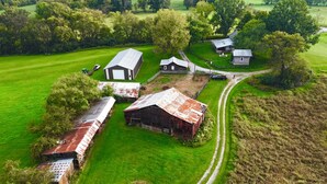 An aerial view of a rural property with barns, a dirt road, and surrounding greenery.