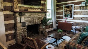 A log cabin interior with a stone fireplace, wooden furniture, and a television mounted above it.