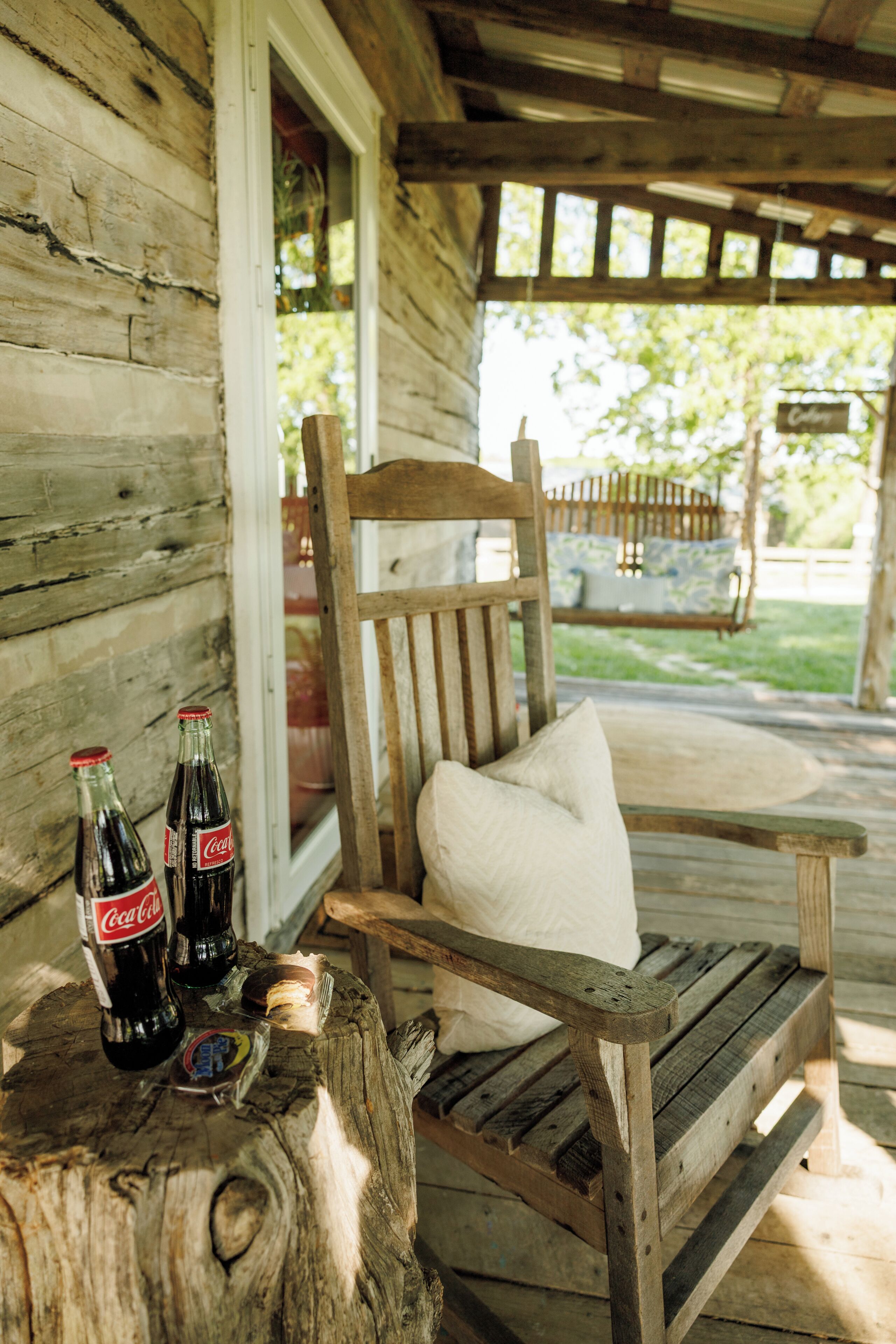 A wooden bench with a cushion, two Coca-Cola bottles, and a wooden stump.