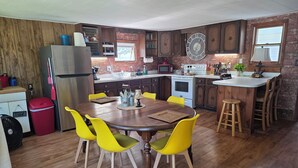 A kitchen with wooden cabinets, a stainless steel refrigerator, a microwave, a stove, and a sink. There is a dining table with yellow chairs and a red trash bin. - Large Cottage:  Private Beach/Stunning Sunsets/Kayaks/Fire Pit (Swanton)